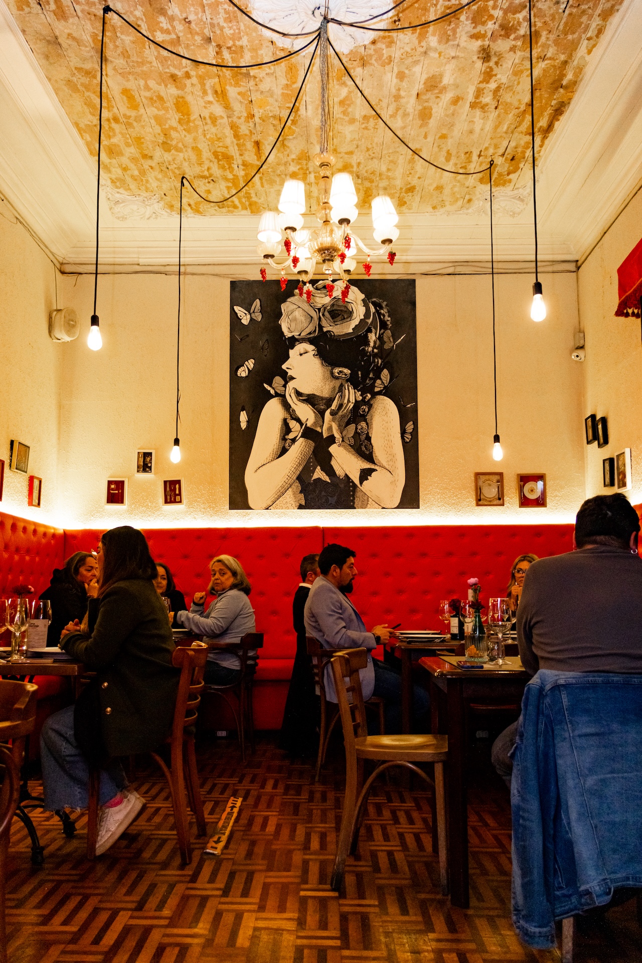Salón de Casalegre: cielo alto descascarado, araña de cristal, mural y sofás de terciopelo rojo